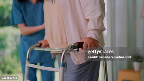 caregiving nurse helping senior patient walking with a crutch after recovery. - mobility walker stock pictures, royalty-free photos & images