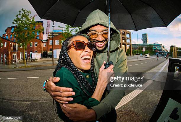 young couple sharing umbrella and laughing in the city - real couple stock pictures, royalty-free photos & images