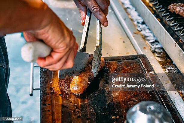 maestro de la parrilla using a knife to slice chorizo sausage for argentine choripan, a street food sandwich with chorizo sausage and chimichurri - chorizo stock pictures, royalty-free photos & images