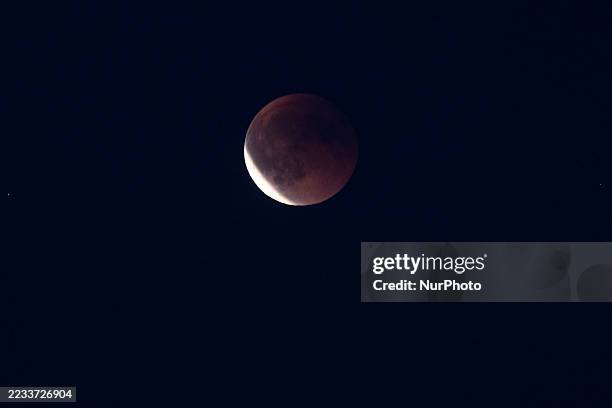 Total lunar eclipse over Europe. A rare blood moon appears rising in the night sky during the eclipse over and behind residential buildings, near the...