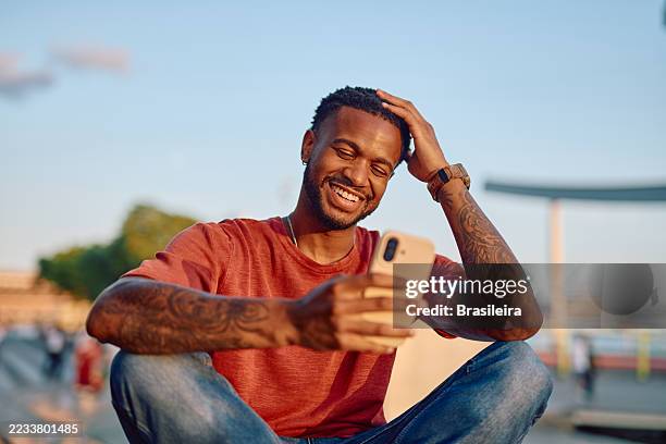 jeune homme riant en utilisant un téléphone portable à l’extérieur - représentation masculine photos et images de collection
