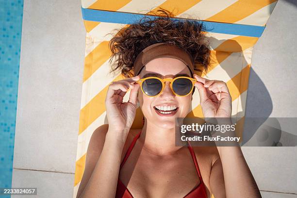 smiling woman in sunglasses relaxing on a poolside sun lounger - stralende lach stockfoto's en -beelden