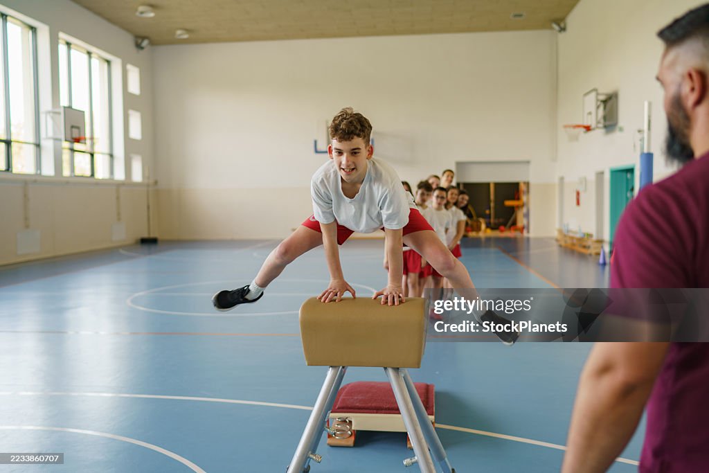 Elementary age boy jumping over pommel horse during gymnastics class
