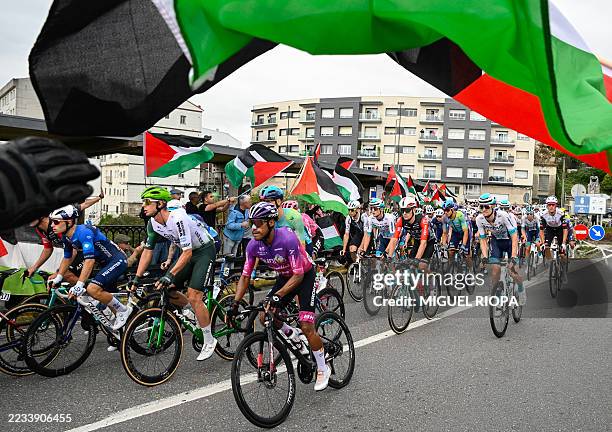 Pro-Palestinian protesters wave flags and shout as the peloton rides by in Poio at the start of the 16th stage of the Vuelta a Espana, a 172 km race...