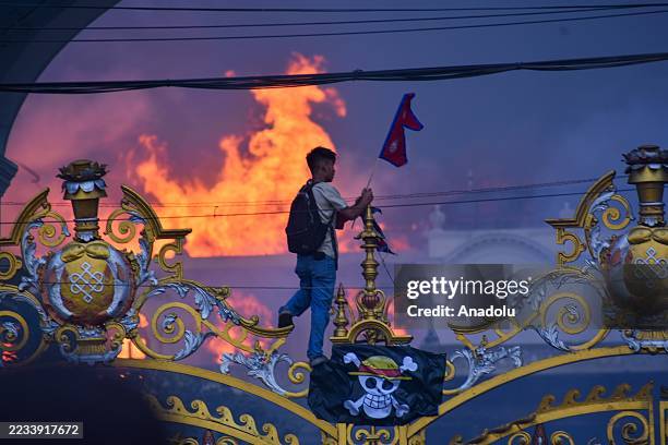 Man is hanging a pirate flag as smoke and flames rise from the Singha Durbar after people set fire to the Singha Durbar, the seat of Nepal...
