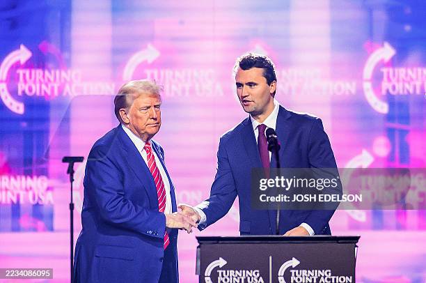 This photo taken on December 22, 2024 shows right-wing activist Charlie Kirk shaking hands with US President Donald Trump as he speaks on stage at...
