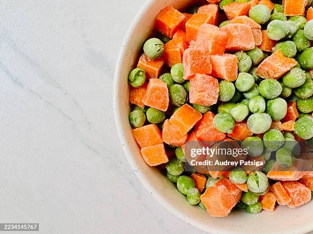 frozen peas and carrots in white bowl with white space for text - aliment surgelé photos et images de collection