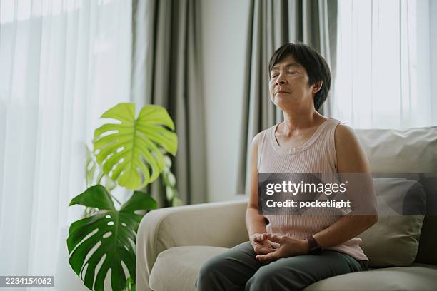 mujer madura meditando pacíficamente en casa. - buena postura fotografías e imágenes de stock