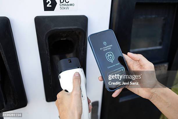 persona que usa un teléfono inteligente para controlar la carga de vehículos eléctricos en la estación - movilidad sostenible fotografías e imágenes de stock