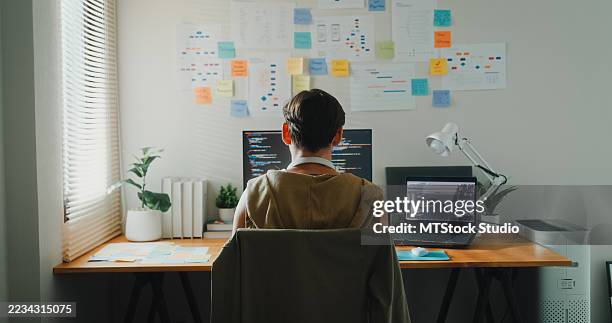 young gay computer programmer working on ai prompts and web page designs coding user experience on laptop in bedroom at home. software developer, artificial intelligence and programming. - javascript stock pictures, royalty-free photos & images