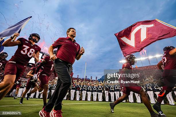 Head coach Brent Pry of the Virginia Tech Hokies runs onto the field with Kyle Lowe of the Virginia Tech Hokies carrying the Virginia state flag...