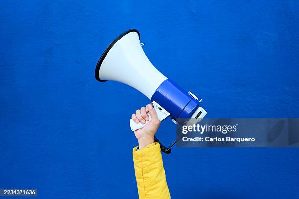 hand holding megaphone on yellow background making announcement. - megafono fotografías e imágenes de stock