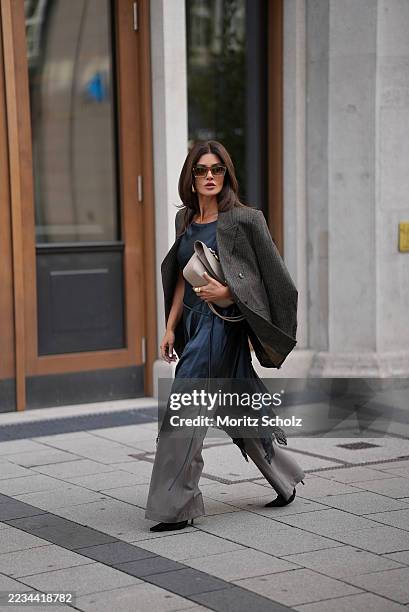 Füsun Lindner is seen wearing a dark grey, double-breasted blazer draped casually over the shoulders from Isabel Marant Etoile; a flowing navy silk...