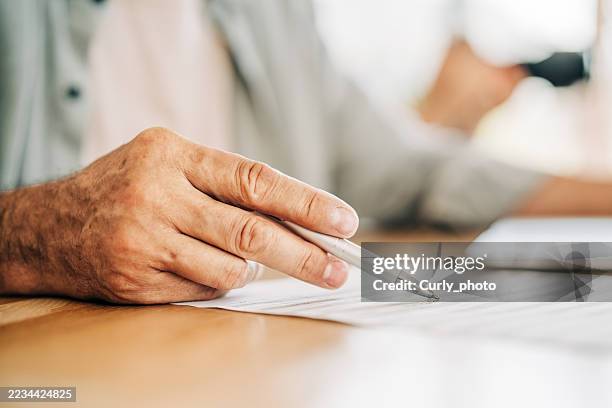 a close-up shot of an older person's hand holding a pen, pointing at a document or contract. the moment of decision-making, such as signing a contract or reviewing documents. - erfenis stockfoto's en -beelden