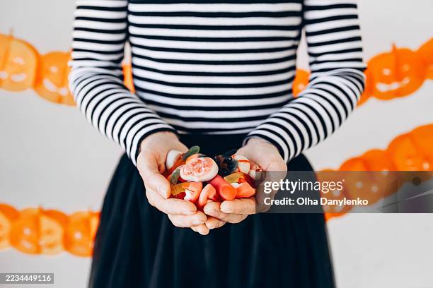 female hands holding assorted halloween gummy candies shaped like eyeballs, worms, fingers and spooky treats - grote groep dingen stockfoto's en -beelden