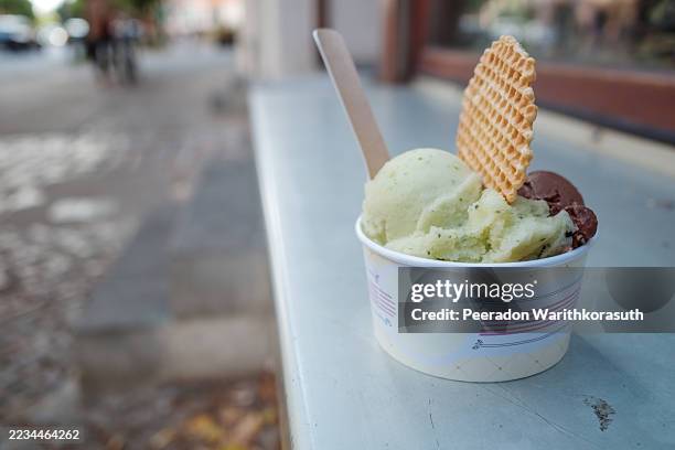 a paper cup of artisanal gelato sits on an outdoor ledge on a city street. - gelato stock pictures, royalty-free photos & images