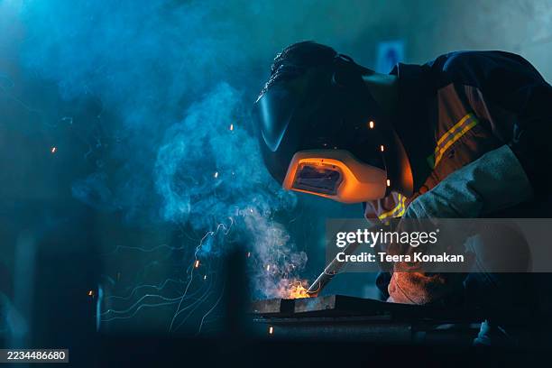 professional welder wearing a dark helmet and gloves welds steel - welding helmet stock pictures, royalty-free photos & images