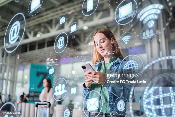 femme adulte moyenne utilisant un téléphone portable et regardant des données sur la réalité augmentée à l’aéroport - hologramme photos et images de collection