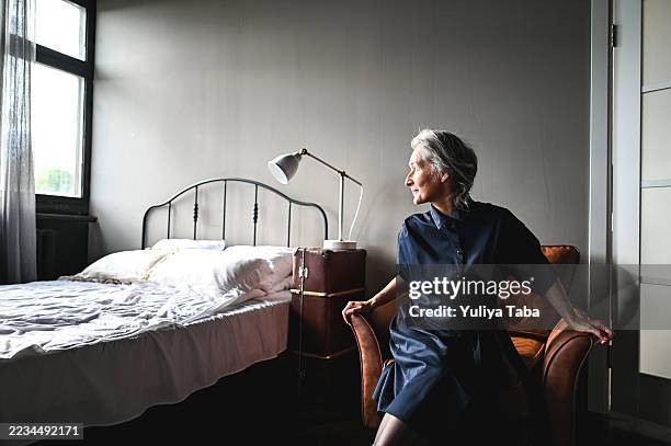 senior woman relaxing in bedroom, gazing out window - widow stock pictures, royalty-free photos & images