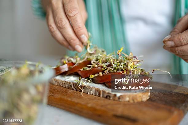 person's hands carefully adding sprouts to a slice of bread topped with tomato slices and a spread. - superfood stock-fotos und bilder