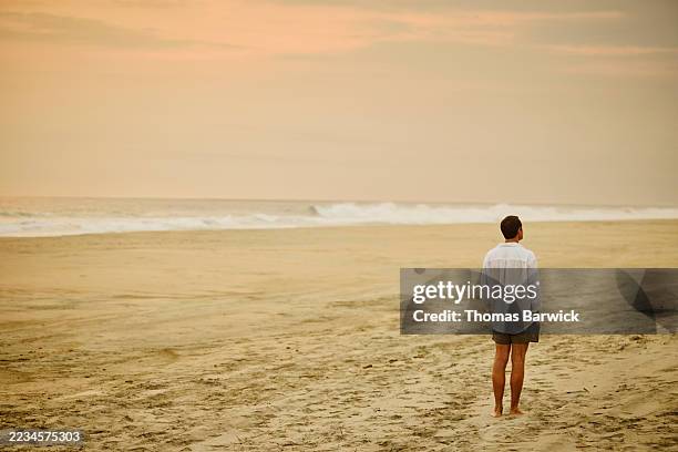 wide shot man standing on empty beach looking at view during sunset - plano geral imagens e fotografias de stock