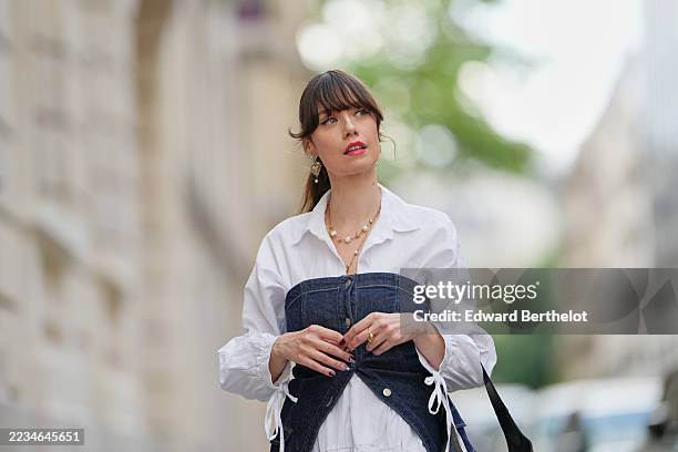 Marion Felicite wears brown hair styled in a ponytail with bangs, pearl drop earrings, a black leather Alexander McQueen shoulder bag, a white...