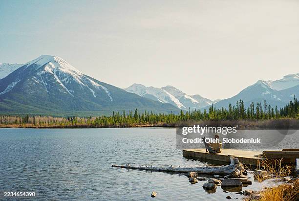 man sitting with the dog at lake in banff national park during getaway in summer, shot on film - canadian rockies stock pictures, royalty-free photos & images