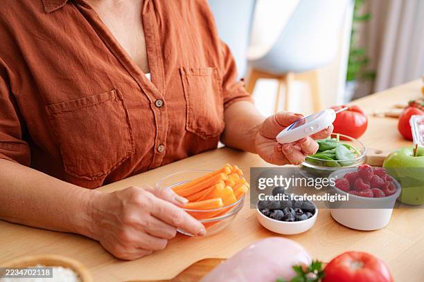 donna irriconoscibile che legge i risultati del livello di glucosio nel sangue utilizzando un glucometro. gli ingredienti alimentari sani raccomandati per i pazienti diabetici sono in tavola - ormone foto e immagini stock