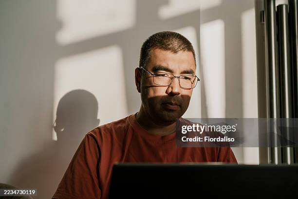 man working on laptop with natural light and shadow effects - gaming laptop stock pictures, royalty-free photos & images