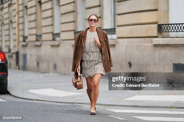 Diane Batoukina wears sunglasses by Kaleos, a brown suede blazer jacket by Source Unknown , a gray fringed tiered boho style mini dress by Michael...