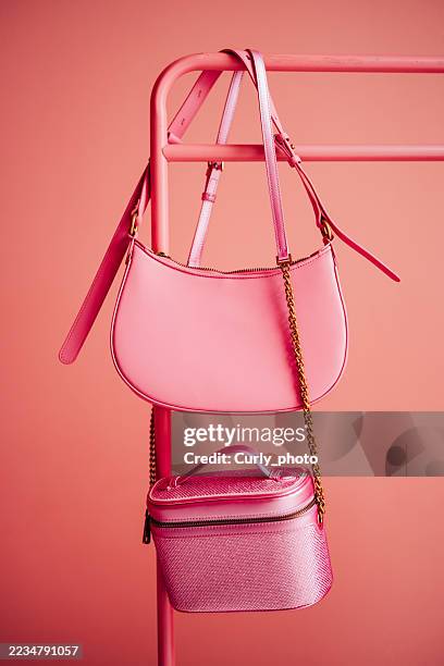 two trendy pink handbags, one glossy and one glittery, hang from a matching pink metal rack against a pink monochromatic background. this stylish still life highlights fashion accessories, current trends, and the vibrant use of color. - composición fotografías e imágenes de stock