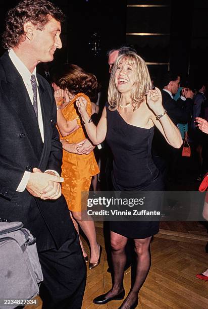 American actress and comedian Teri Garr, wearing a black asymmetric dress, dances with a man who wears a black suit over a white shirt with a...