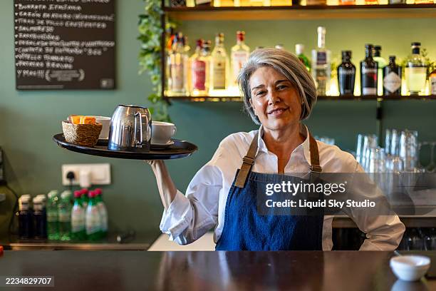 camarera madura sosteniendo bandeja con café y leche en la cafetería - camarera fotografías e imágenes de stock
