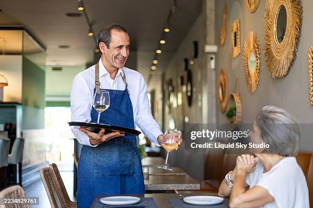 camarero senior sirviendo vino a una mujer madura en un restaurante - camarero fotografías e imágenes de stock