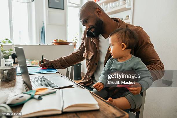 cute baby boy sitting with father working from home - multitasking stock-fotos und bilder
