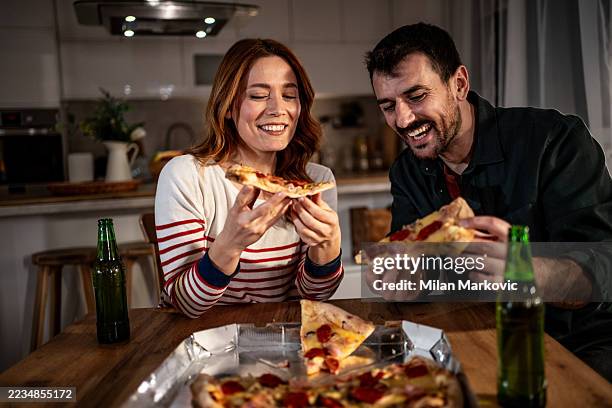 happy couple enjoying pizza and beer at home - couple sharing food stock pictures, royalty-free photos & images
