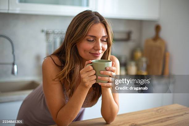 serene woman enjoying a cup of coffee in her kitchen - aromatherapy stock pictures, royalty-free photos & images