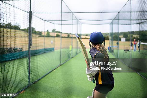 back view through net as young female batsman stands ready to hit the ball - cricket player stock pictures, royalty-free photos & images