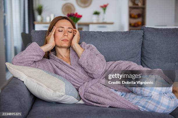 frau, die unter starken kopfschmerzen leidet und zu hause auf dem sofa liegt - symptom stock-fotos und bilder