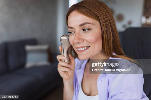 smiling woman using electric microcurrent facial massager at home - exfoliation stock pictures, royalty-free photos & images