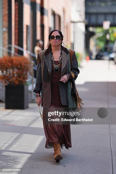 Guest wears dark hair pulled back with a center part, black rectangular sunglasses, layered chunky chain necklaces in mixed silver- and gold-tone...