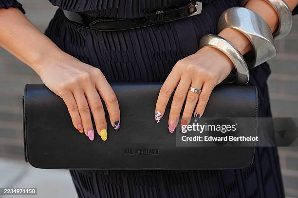 Samia Laaboudi wears stacked silver large cuff bracelets and a ring, a structured black leather clutch with a flap, a navy ribbed knit shirt dress...