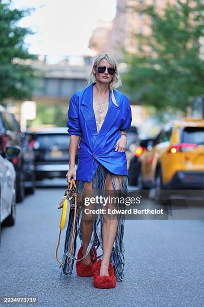 Guest wears blonde hair in a low side ponytail, black rectangular sunglasses, a small brown monogram coated canvas top handle bag from Louis Vuitton...