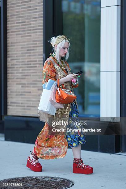 Guest wears platinum-blonde hair pulled into a loose updo with a gold sequined headscarf, layered green and gold beaded necklaces and green drop...