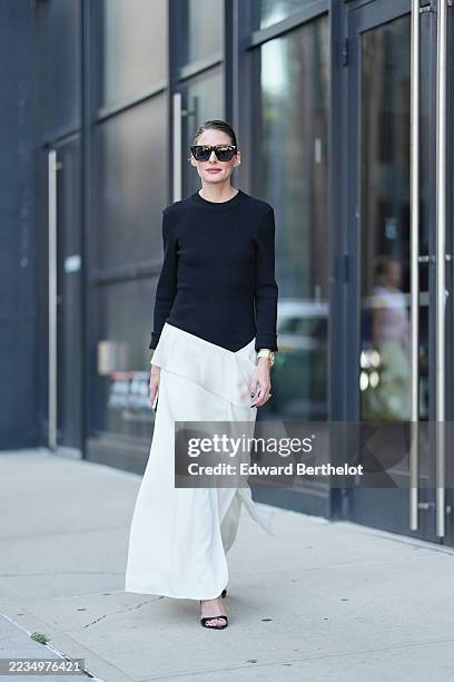 Olivia Palermo wears hair pulled back into a low bun, black oversized cat-eye sunglasses, a gold metal wristwatch on the left wrist, a fitted black...