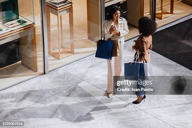 two elegant businesswomen chatting after shopping in a luxury store - buying stock pictures, royalty-free photos & images