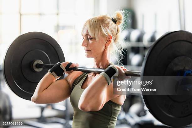 focused mature female athlete lifting heavy barbell during cross training workout - tyngdlyftning bildbanksfoton och bilder