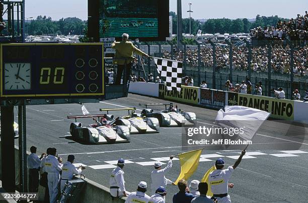 Emanuele Pirro of Italy driving the Audi Sport Team Joest Audi R8 Audi V8 raises his arm to take the chequered flag at the finish alongside 2nd place...