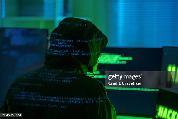 rear view point hooded hacker coding in secret location.hooded hacker coding in secret location - computerhacker stock-fotos und bilder