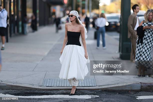 Coco Schiffer seen wearing narrow black cat-eye sunglasses, white lace headscarf, strapless black-and-white long dress featuring a fitted black...
